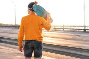 Young man with a longboard on a bridge at sunset