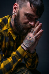 Close up portrait of a bearded man with tattoos on his hands and neck wearing yellow black shirt.