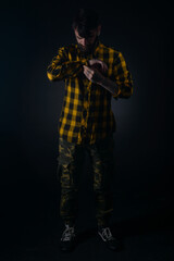 Dark image of a bearded man with tattoos fixing his buttons on his yellow and black checkered shirt