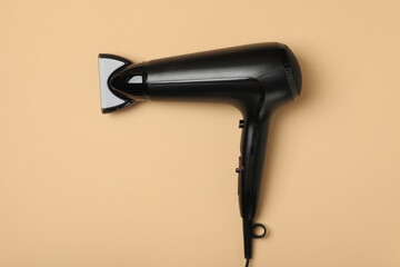Black hair dryer on beige background, space for text