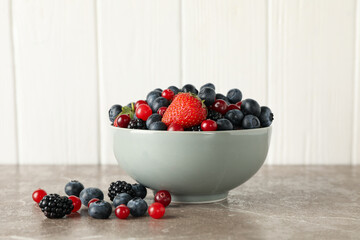 Bowl with fresh berries on gray table, space for text
