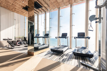 Gym fitness and Treadmill equipment at sky sea view and sunlight, on top modern  condominium overlooks the sea,  The sun's rays penetrated the big window into the luxury gym.