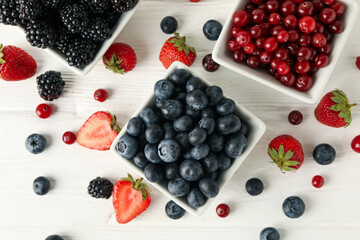 Bowls with berries on white wooden background, top view