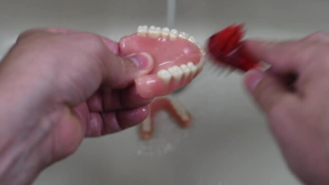 denture cleaning with brush in the sink with running water