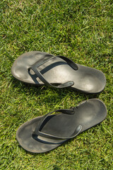 A pair of black rubber flip-flops on the green lawn grass with a copy of the space, summer,...