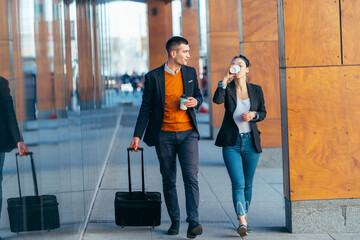 Business couple ( colleagues ) walking along the futuristic modern station (airport) while drinking coffee and talking to each other.