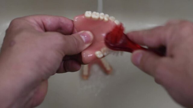 denture cleaning with brush in the sink with running water