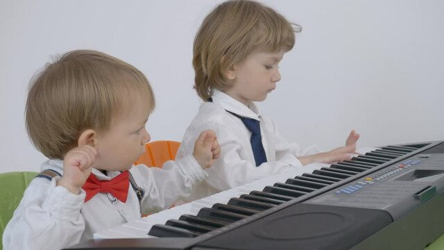 Amusing baby child and brother have fun , play at piano, dance, teamwork, elegant children with tie and bow love classical music