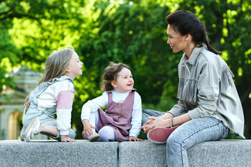 Happy mother and her two daughters sitting and playing in a city park