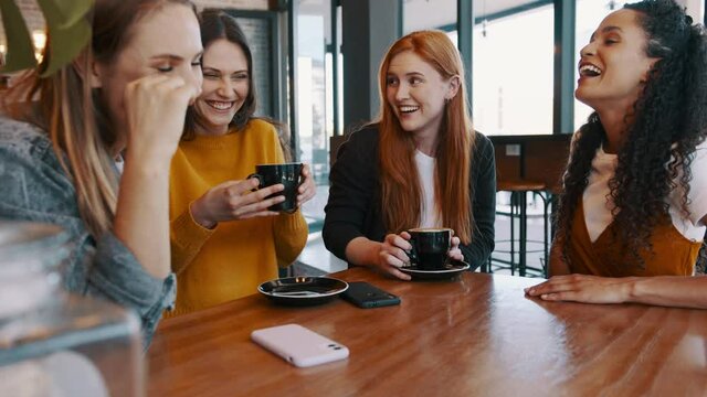 Group of female friends chatting at a cafe. Four women meeting in a coffee shop and talking.
