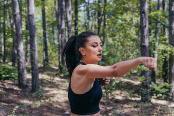 Close up portrait of a sexy brunette exercising kickbox with direct punches in the middle of the forest