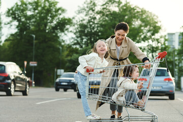 Happy mother and her daughters are having fun with a shopping cart on a parking lot beside a supermarket. © blackday