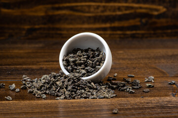 loose black tea next to a cup of tea on a dark wooden background