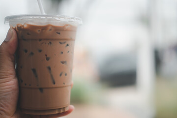 Hand holding iced mocha with straw in plastic cup