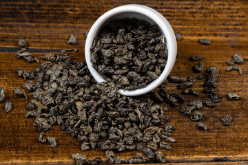 loose black tea next to a cup of tea on a dark wooden background