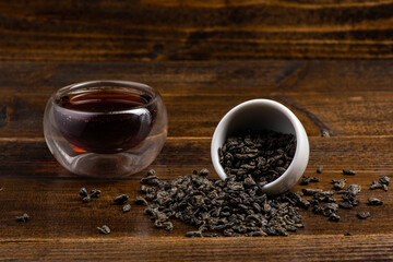 loose black tea next to a cup of tea on a dark wooden background