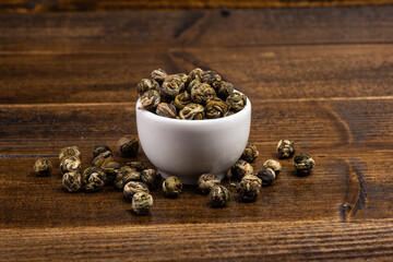 green tea sprinkled next to a cup of tea on a dark wooden background