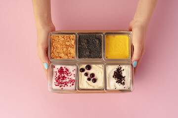 Mousse desserts in square plastic boxes with different toppings on pink table