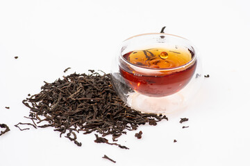 loose black tea next to a cup of tea on a white background