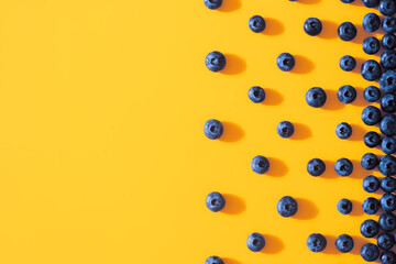 Fresh sweet blueberry fruit on colorful yellow background. Dessert healthy food concept. Raw summer diet. Delicious nature vegetarian ingredient. Flat lay, minimal style, copy space