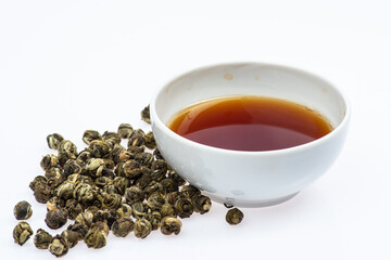 loose green tea next to a cup of tea on a white background
