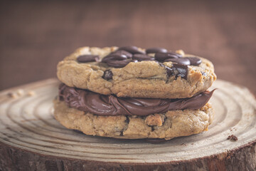 sanduíche de cookies frescos com nutella cremosa em cima de uma tábua de madeira com fundo escuro, isolada