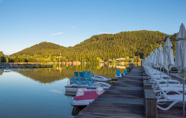 A view of a mountain alpine lake on a evening. Lake with hills, water and blue sky with clouds. Green forest by the lake in reflection in the water beauty in nature