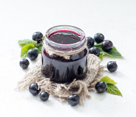 Black currant jam in a jar on a light background in rustic style