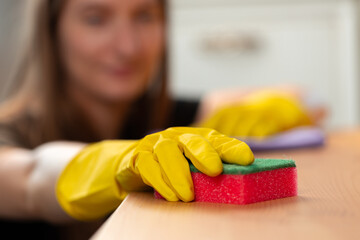 Unrecognizable woman in yellow gloves wiping wooden table top