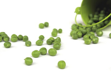 Overturned green bucket with green peas scattered on a white surface