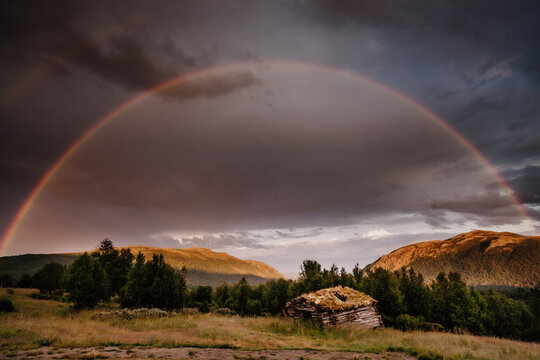 Scenic view of rainbow over mountains with hut in foreground