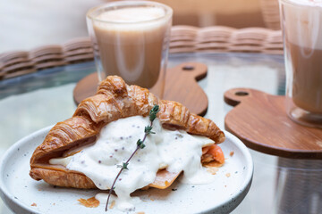 Homemade Croissant with Eggs Benedict, ham and salmon in plate for breakfast. Croissant Sandwich. Fresh baked croissant stuffed with smoked salmon, poached egg, fresh ham and homemade sauce.