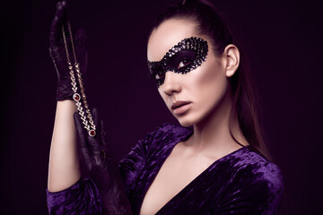 Elegant brunette woman in sequins mask with black gloves looks at diamond necklace