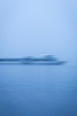 Long exposure vertical action shot of ghostly moving boat figure, gliding from left to right on the waters of a lake, during a cold winter evening