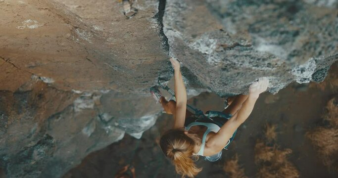 Attractive woman rock climbing up cliff face, cinematic slow motion, fitness lifestyle