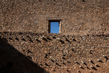 Ruin of Mexican hacienda. Large stone wall with tiny square window that looks out into clear blue sky. Horizontal full frame view of stone texture of building from the 1900s in Guanajuato