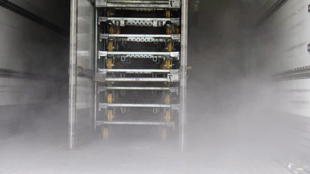 Ice cold mist blowing from freezer of refrigerated trailer of truck. Transporting food and drink both frozen and chilled. Technology used by food produce industry. Steel metal trolley wheels stacked