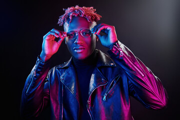 Futuristic neon lighting. Young african american man in glasses standing in studio