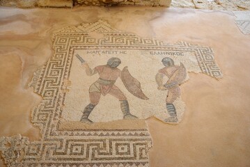 Detail from the damaged mosaic floor with two gladiators and their names above the heads saying Margarites and Hellenikos in Greek at the Neolithic period Kourion Ancient city in Cyprus