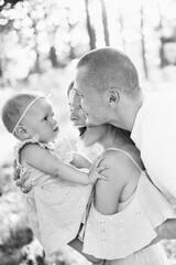 Portrait of young parents smiling to beautiful daughter, hugging, lovely family walking at the park, caring mother holds cute baby girl, enjoy happy moments, weekend outdoors, childhood concept