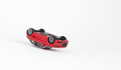 Red rattle toy car, turned over on the roof as a result of an accident. White copy space background.