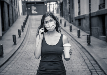 Fototapeta premium Woman wearing surgical protective face mask talking on mobile phone in public space in the city