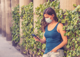 Woman wearing surgical protective face mask talking on mobile phone in public space in the city