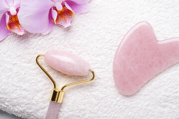 Rose Quartz jade roller and Gua Sha massager on towel on stone background. Close-up. Massage tool for facial skin care, SPA beauty treatment concept