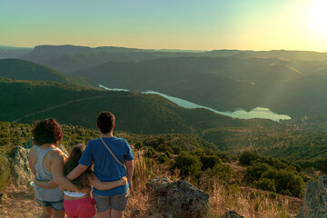 Fototapeta premium A woman with her children, a boy and a girl, watching from the top of the valley the mountains and the Douro River as the sun sets at dusk. Vilvestre, Spain