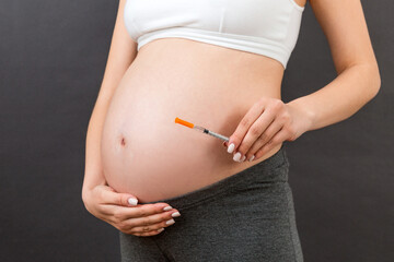 Close up of pregnant woman holding insulin syringe against her belly at colorful background with copy space. Diabetes concept