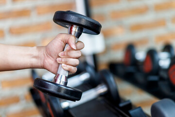 Closeup a man's hand holds a dumbbell with his right hand in the gym.