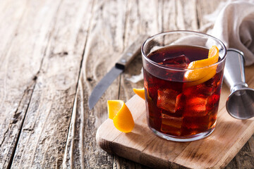 Boulevardier cocktail and orange zest on wooden table. Copy space