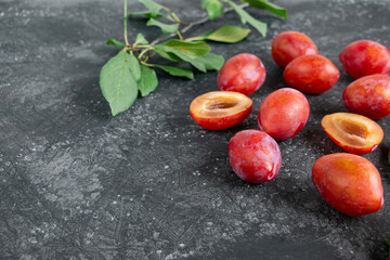 Ripe plum (cherry plum) and green leaves on the branches on a dark background. Still life in a dark key. Simple layout with copy space for text.