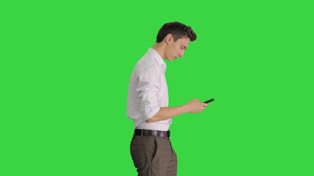 Man In White Shirt Walking Using Cell Phone On A Green Screen, Chroma Key.